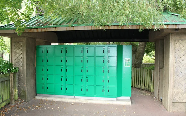 Archive photograph of green theme-park lockers beneath a small roof beside trees and a path.
