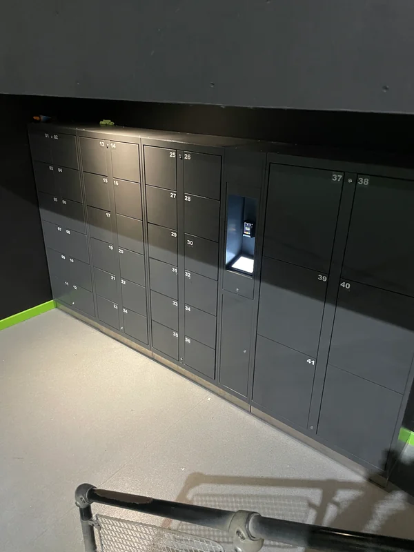 Grey self-service lockers with small and large compartments and a recessed kiosk at a trampoline park.