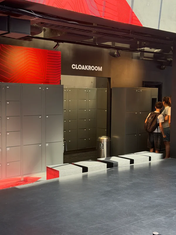 Visitors beside grey self-service lockers and cloakroom seating in a museum.