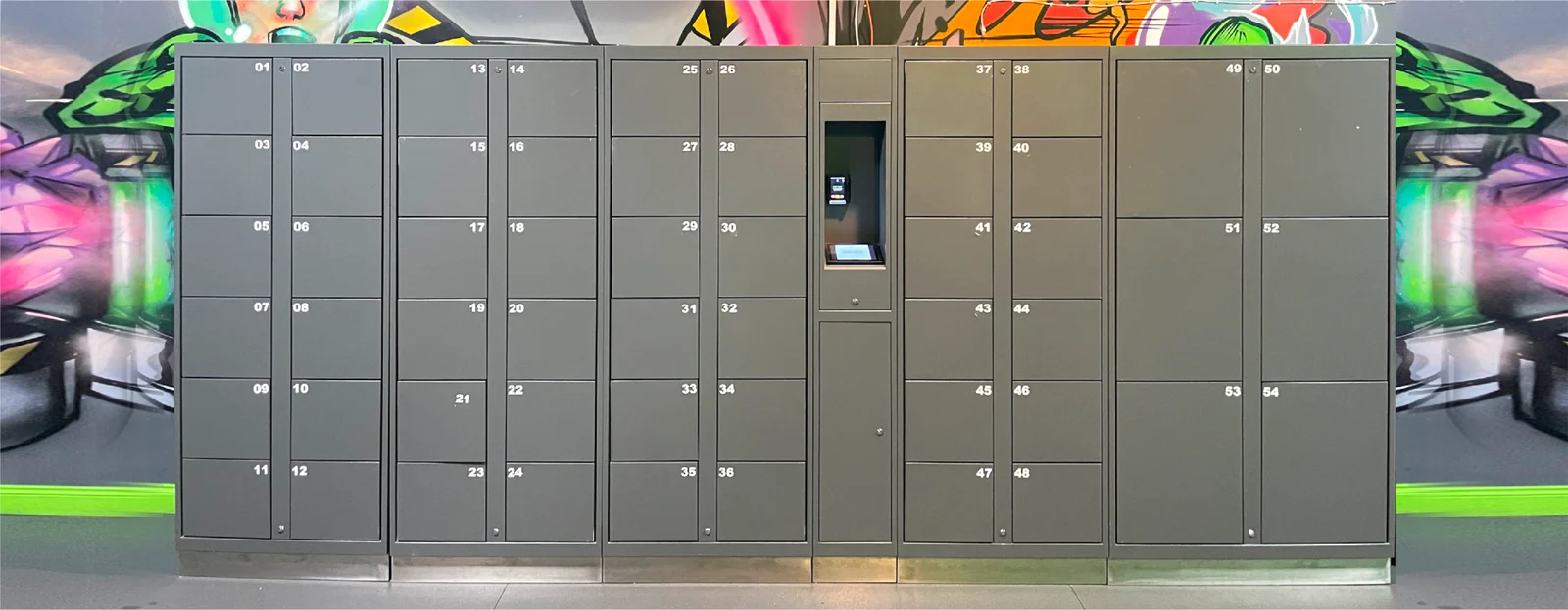 Front view of grey pay-per-use lockers with different compartment sizes and an integrated touchscreen kiosk