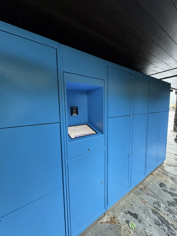 Blue theme-park lockers with a touchscreen and card-payment terminal beneath a timber roof.