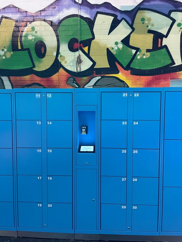 Card-payment terminal and touchscreen between numbered blue theme-park locker doors.