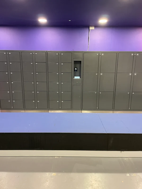 Grey trampoline park lockers with mixed compartment sizes and a central kiosk beside seating.