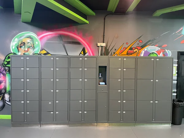 Grey trampoline park locker bank with a touchscreen and card reader against a colourful mural.